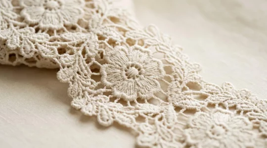 Gros plan sur un tissu en guipure structuré aux motifs floraux ajourés avec brides visibles, éclairage naturel doux créant du relief et des ombres sur la texture complexe